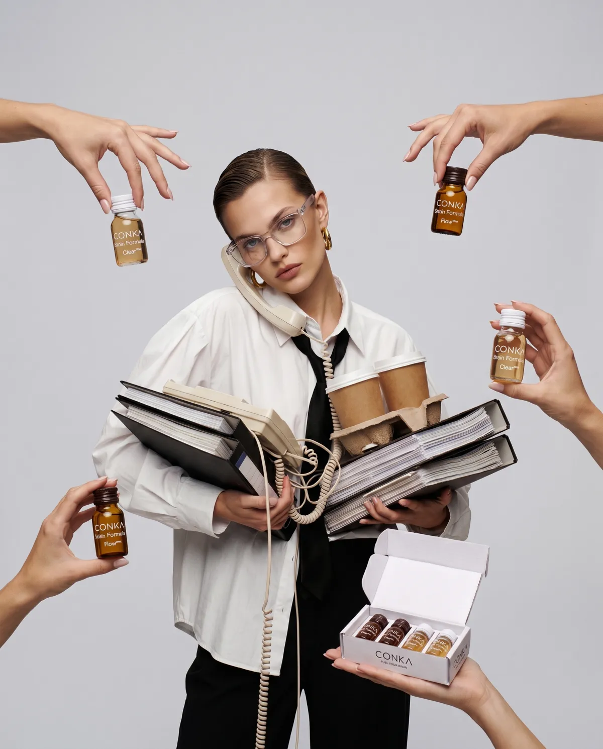 A woman on the phone with arms full of folders and coffees, as hands offer her CONKA shots from every side