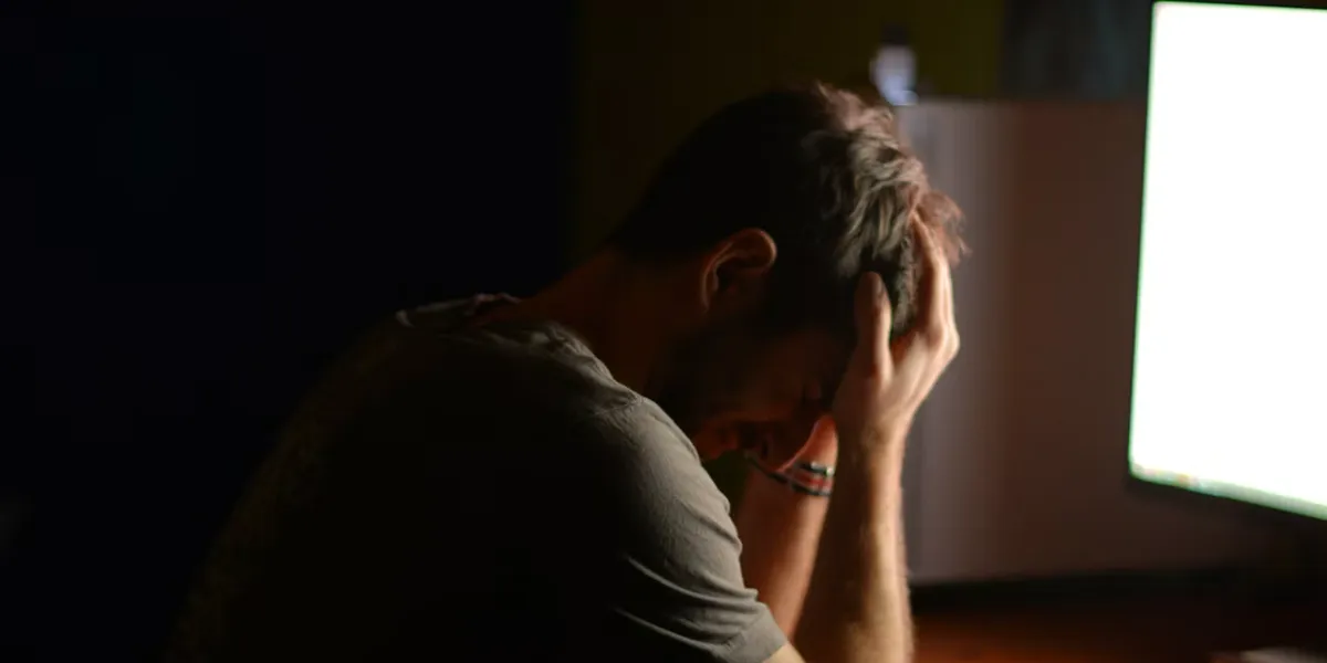 A man at a desk in a dark room with his head in his hands