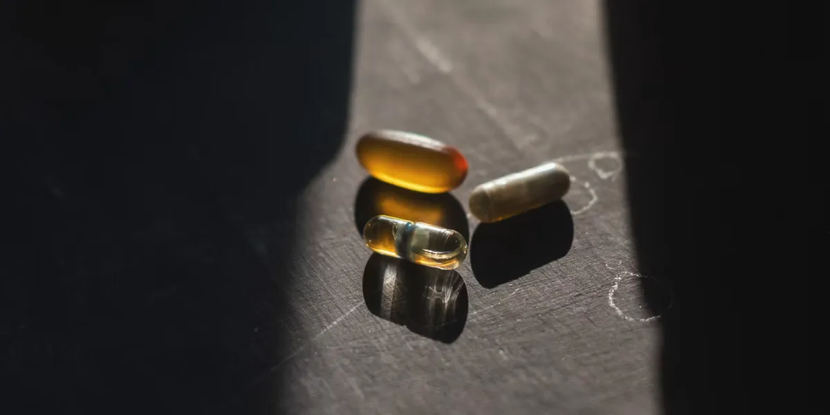 A few supplement capsules lying in a strip of light on a dark table